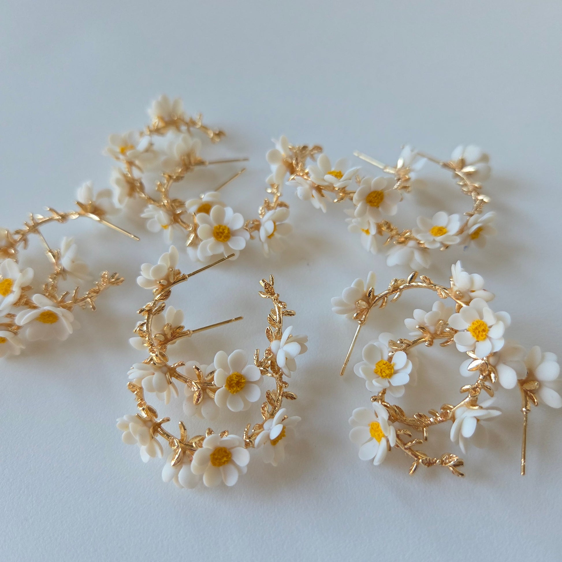 Gold hoop earrings with white floral accents on a light gray background