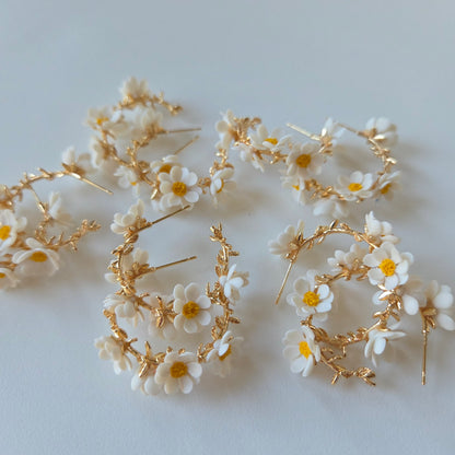 Gold hoop earrings with white floral accents on a light gray background