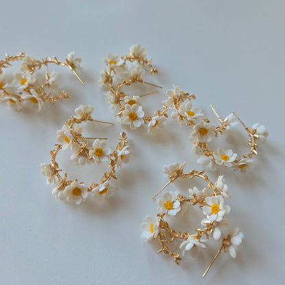 Gold hoop earrings with white floral accents on a light gray background