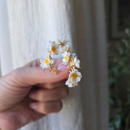 Hand holding a decorative ring with white flowers daisies and gold accents against a blurred background