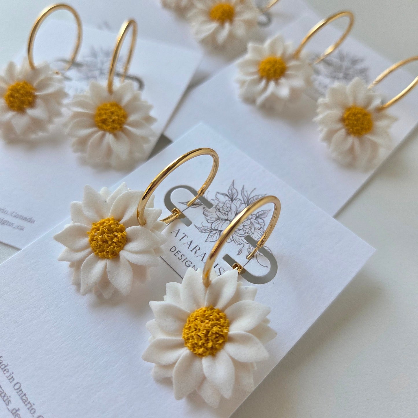 Gold hoop earrings with white floral details on a white card