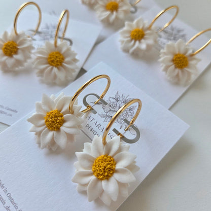 Gold hoop earrings with white floral details on a white card