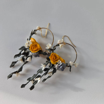 Floral earrings with yellow roses and green leaves on a light gray background
