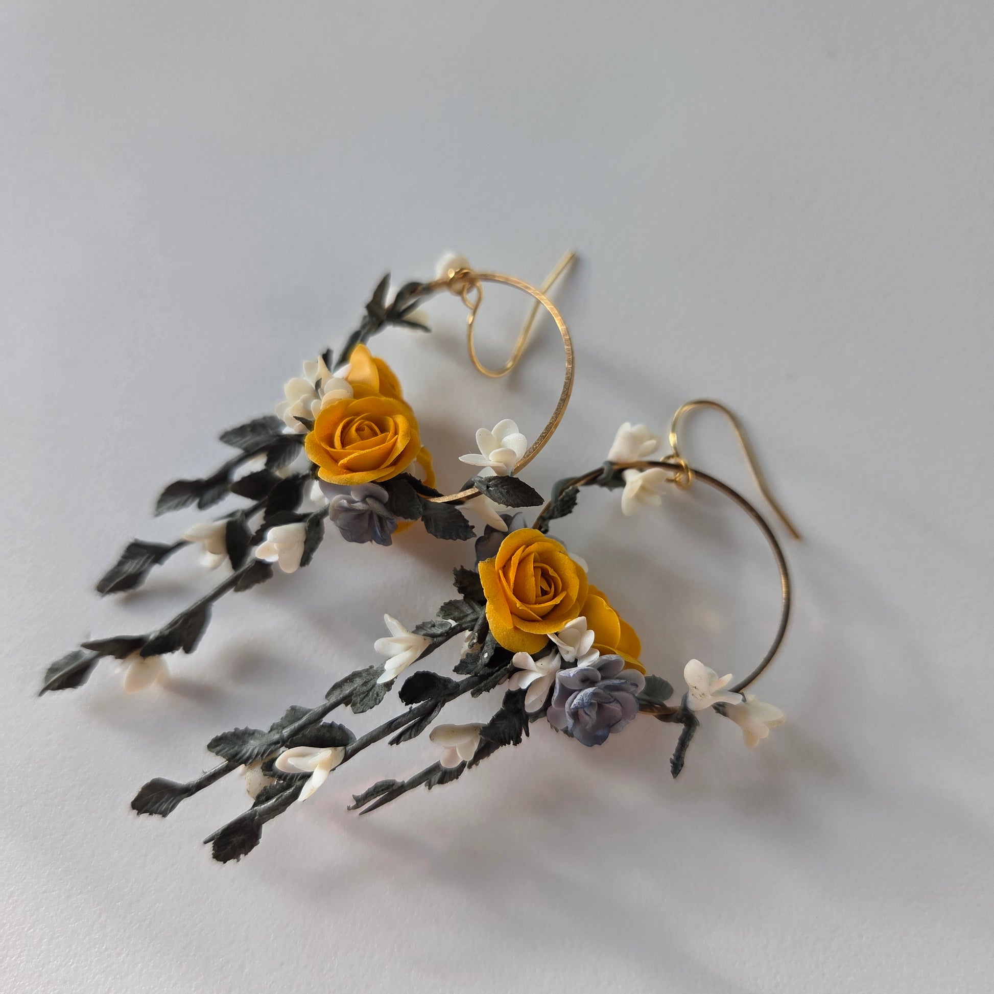 Floral earrings with yellow flowers and green leaves on a light gray background