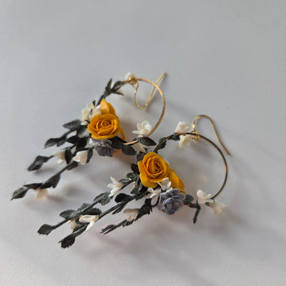 Floral earrings with yellow flowers and green leaves on a light gray background