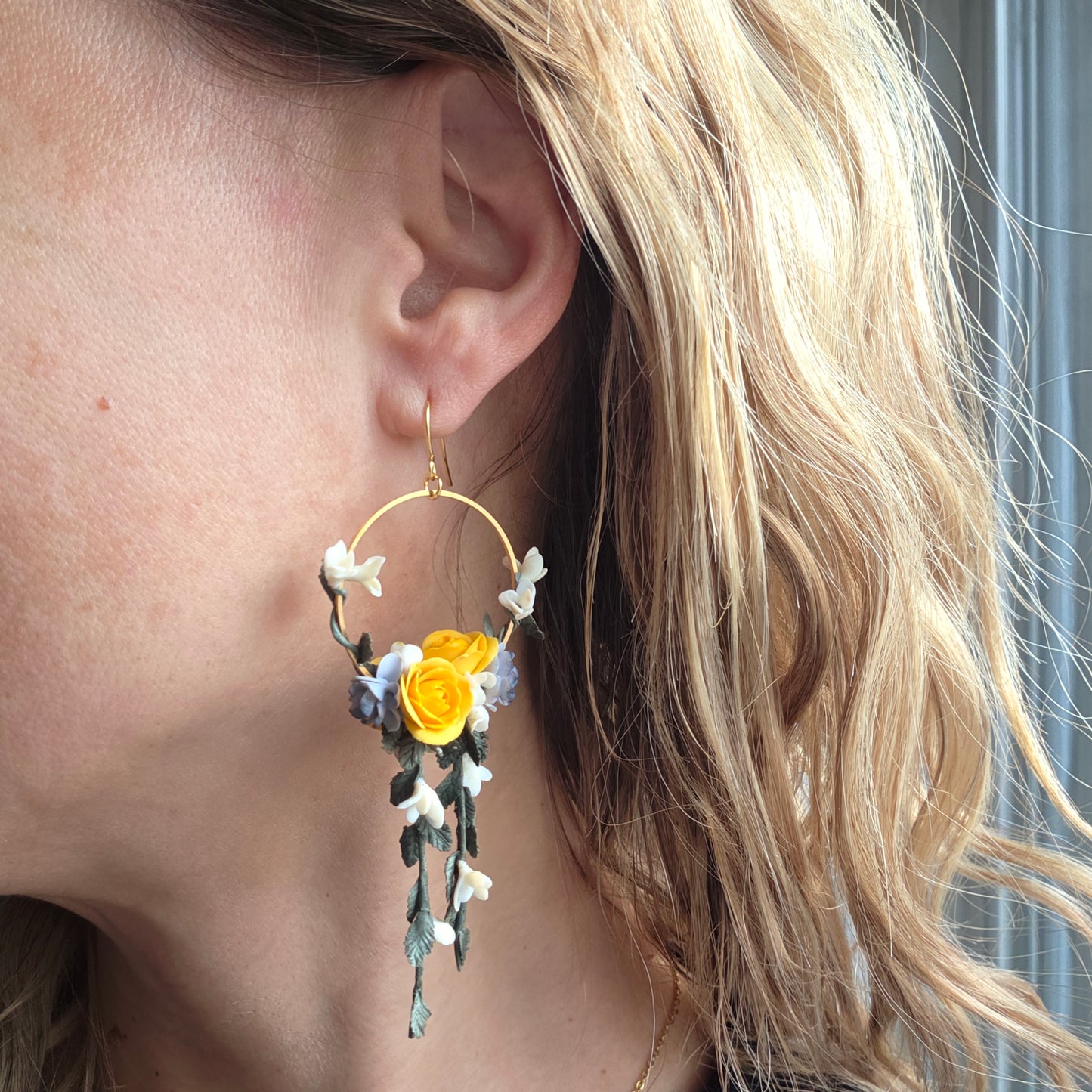 Close-up of an ear wearing a floral earring with yellow flower and green leaves.