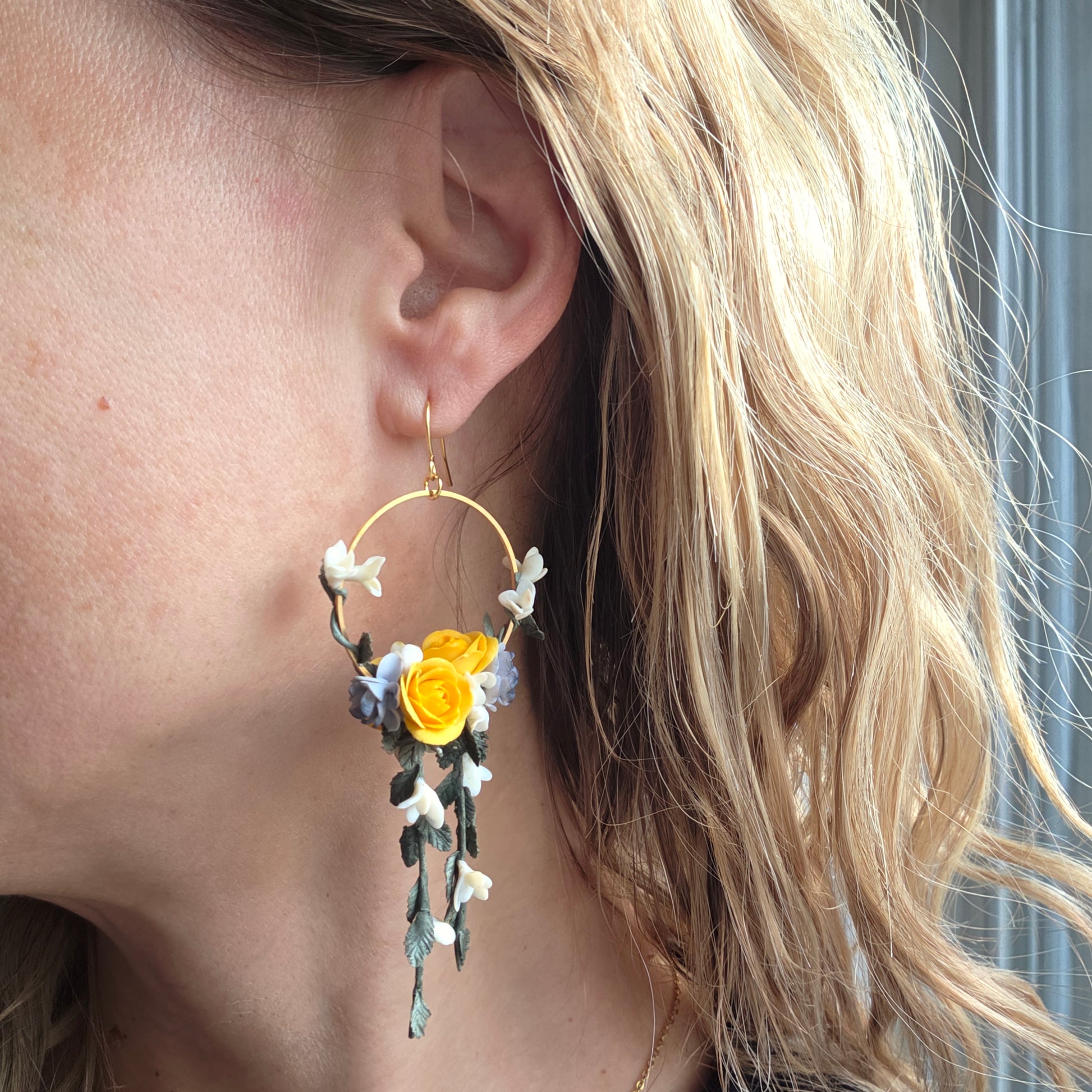 Close-up of an ear wearing a floral earring with yellow flower and green leaves.