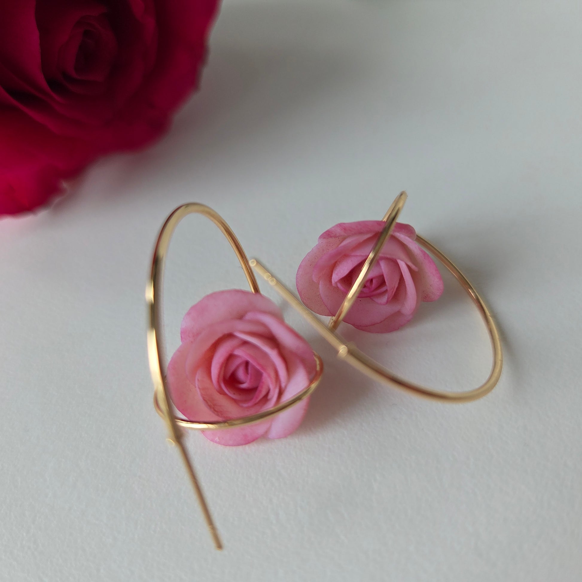 Gold hoop earrings with pink roses on a white background