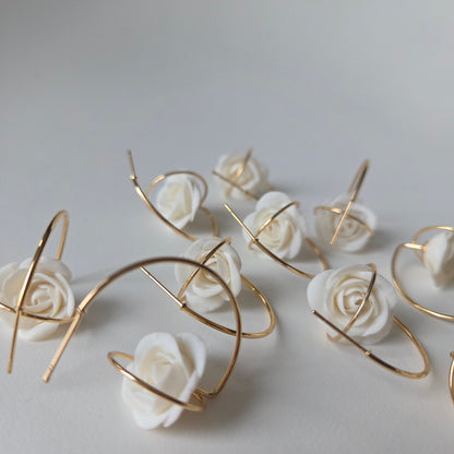 Gold hoop earrings with white rose details on a light gray background