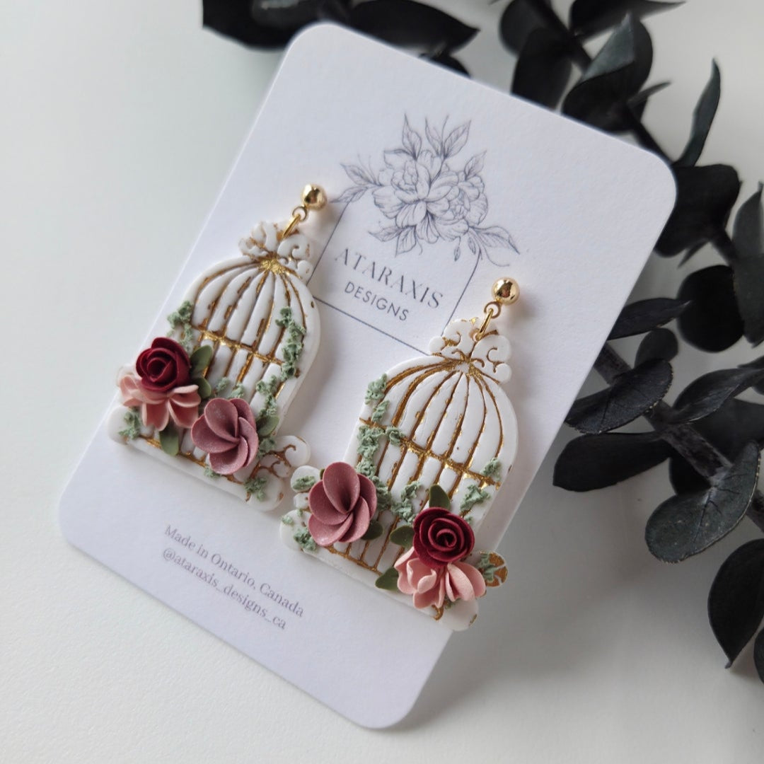 Decorative earrings on a branded card with black leaves in the background
