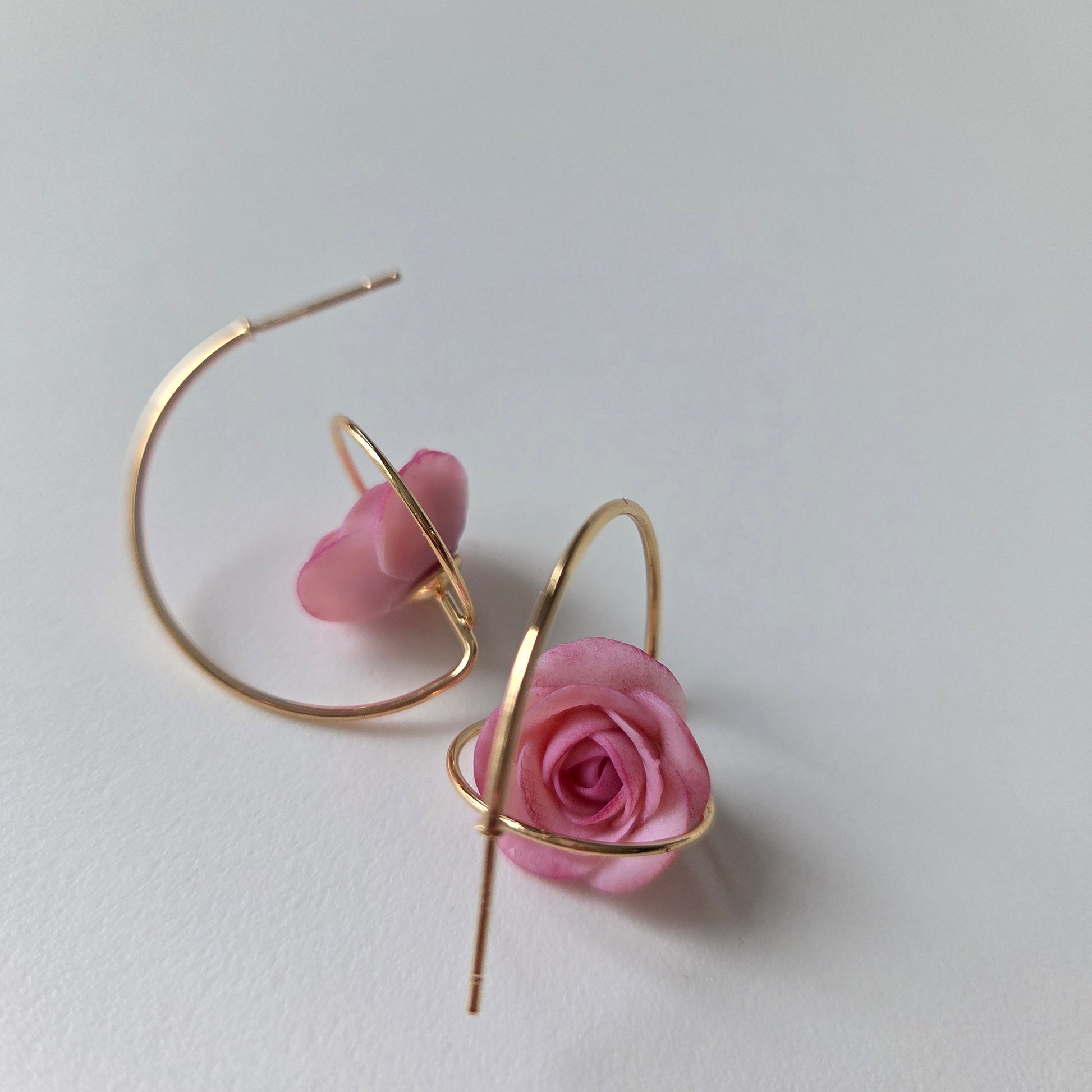 Gold hoop earrings with pink rose petals on a light gray background